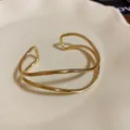 Elegante primo piano di un bracciale a fascia dorato multistrato su piatto bianco - Onda Multistrato / Oro