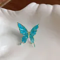 Detailed macro view of a delicate blue enamel butterfly ear clip resting on a white shell - Blue