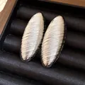 Detail of vintage oval silver-tone earrings with textured ribbed surface on black jewelry tray. - Silver
