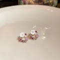 Elegante Blumenkranz-Ohrstecker mit weißen Blüten und rosa Steinen auf einem Teller - Rosa Hohler Kranzstil
