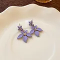 Dettaglio di orecchini a pendente con fiori viola opaco su un piatto di ceramica bianca. - Viola