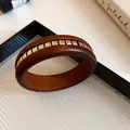 Detailansicht eines Holzarmreifs mit quadratischen Metalleinlagen in einem Tablett - Armreif-Kaffee