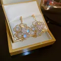 Elegante goldene Perlenblumenohrringe mit irisierenden Kristallen in Schmuckschatulle - Irisierendes Kristall Hohlblütenblatt-Stil