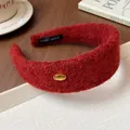Macro view of a luxury red flocked wide headband with a gold KOREA emblem on a wooden desk. - Brown