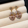 Detailed macro view of elegant pink and lavender crystal dangle earrings in a beige box - Pendant Styles / Gold-Purple