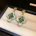 Detailed view of vintage gold floral earrings with white petals and green enamel in box - Green And Gold (Silver Post)