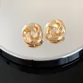 Close-up of elegant gold twisted knot stud earrings on a mirrored reflective surface - Twisted Flower Design / Gold
