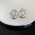 Close-up of silver metal rose knot stud earrings with a high-polished metallic finish. - Twisted Flower Design / Silver
