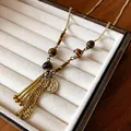 Close-up detail of vintage ceramic beads and metal coin pendant on long tassel necklace - Gold-Khaki