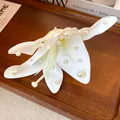 Close-up of white fabric lily hair clip with elegant pearl embellishments on petals. - White