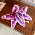 Detail shot of a purple fabric lily hair clip with white pearls on a wooden tray. - Purple