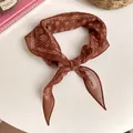 Detalle de un pañuelo vintage marrón con estampado paisley anudado sobre fondo blanco - Marrón