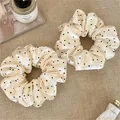 Close-up of elegant cream satin scrunchies featuring classic black polka dot patterns - Scrunchie / White Polka Dot