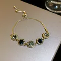 Close-up of elegant gold drawstring bracelet with dark blue and emerald green zircon stones. - 3. Real Gold Plated With Gray Diamonds Bracelet.