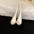 Detailed macro view of minimalist silver teardrop pendant earrings on textured paper - Teardrop / Silver