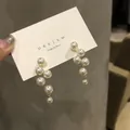 Primo piano di eleganti orecchini a goccia con perle a cascata su carta bianca. - Argento