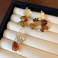 Close-up of asymmetric vintage earrings with amber beads and gold flower studs in a display box. - Asymmetric Flower Tassel Style (HE24112) / Amber Coffee Gold