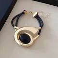 Gedetailleerd zijaanzicht van een gouden spiraalarmband met een zwarte ovale steen. - Armband / Goud-Zwart