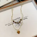 Close-up detail of a layered gold-tone necklace with tiger eye beads and heart pendant - Gold-Brown-Heart
