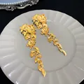 Detailed view of matte gold floral and leaf tassel earrings on a decorative plate. - Long Tassel Flower Leaf Style / Gold