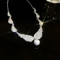 Detailed close-up view of a sparkling silver wing necklace featuring a large white pearl pendant - Necklace (Silver)