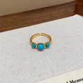 Primer plano de un anillo abierto bañado en oro de 18k con tres piedras turquesas - Estilo de Arreglo de Tres Piedras Redondas Azules (HR2835)