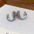 Detailed macro view of textured metallic silver and light blue drip oil C-shaped stud earrings - Silver-Blue
