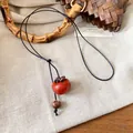 Dettaglio di una collana vintage con pendente a forma di cachi in legno e cordino - Nero e Rosso Cachi