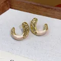 Detailed macro view of gold-tone wrinkled C-shaped stud earrings with pink enamel detail - Gold-Pink