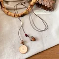 Primo piano di una collana retrò con ciondolo a ghianda e legno su tessuto - Ghianda in Tavola di Legno Marrone