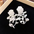 Macro detail view of elegant white floral beaded earrings on black velvet background - Shell Texture Floral Style