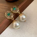 Close-up of vintage gold drop earrings with emerald green gems and white pearls. - Earrings / White