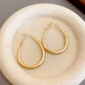 Macro view of minimalist gold-plated U-shaped hoop earrings on a soft textured plate. - Gold