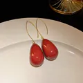 Close-up of elegant red teardrop drop earrings with gold hooks on a white plate - Ear Hook - Water Drop Shape