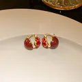 Close-up of red gemstone earrings with a gold-plated finish on a ceramic plate. - Ear Buckle - Half Round Bean Style