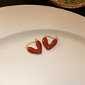 Close-up of elegant red heart hoop earrings with gold-plated finish on a white plate - Ear Buckle - Heart Shape