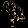 Dettaglio ravvicinato di collane geometriche dorate con maglie rettangolari su sfondo nero. - Stile a Doppio Strato con Ciondolo Geometrico Rettangolare / Oro