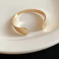 Close-up of a minimalist gold open cuff bracelet with smooth teardrop ends - Plain Polished / Gold