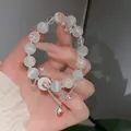 Macro view of a beaded bracelet featuring white cat's eye beads and a silver bell charm. - Moon and Bell Style (32#) / Silver & White