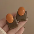Close-up detail of geometric orange and brown resin stud earrings with a glossy finish. - Silver Needle / Brown