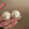 Close-up detail of large white textured dome-shaped stud earrings held in a hand - Silver Needle / White