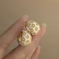 Close-up of elegant flower enamel earrings with sparkling crystal details held by hand - Ear Buckle / Gold-White