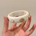Close-up view of a chic cream marble acrylic bangle featuring gold shell and pearl accents - Shell Pearl Bangle / Off White