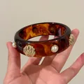 Close-up macro view of tortoiseshell acrylic bangle with shell and pearl embellishments - Marble Pattern Shell Pearl Bangle / Brown