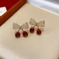 Vue détaillée d'élégantes boucles d'oreilles cerise et nœud avec zircons dans un écrin - Cerise Nœud Papillon (WE5766) / Or-Rouge