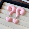 Close-up of pink resin question mark heart drop earrings in a jewelry display tray - Pink
