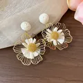 Nahaufnahme eleganter goldener Metall-Blütenohrringe mit kunstvoll gewebten weißen Bastblättern - Blumen-Stil / Khaki