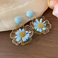 Nahaufnahme hellblauer Bast- und goldfarbener Metall-Blumenohrringe Designdetails - Blumen-Stil / Blau