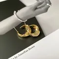 Close-up detail of irregular gold-plated hoop earrings on a magazine background - Gold Textured / Gold