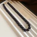 Gros plan détaillé d'un collier de perles marbrées sombres sur un plateau d'exposition - Style Lavis d'Encre Marbre / Noir